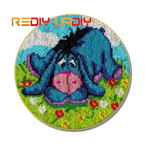 May include: A blue and black needlepoint embroidery of a cartoon donkey with a pink nose and large eyes. The donkey is surrounded by green, yellow, and red flowers.