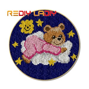 May include: A round needlepoint canvas with a blue background and a white cloud with a pink and brown teddy bear sleeping on it. The canvas is surrounded by a gold trim and has a yellow sun and stars on the background.