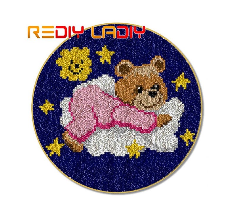 May include: A round needlepoint canvas with a blue background and a white cloud with a pink and brown teddy bear sleeping on it. The canvas is surrounded by a gold trim and has a yellow sun and stars on the background.