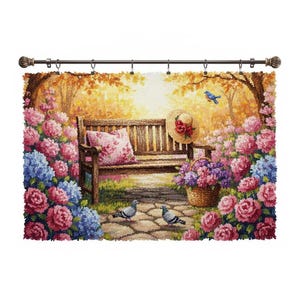 Puede incluir: Un tapiz que representa una serena escena de jardín con un banco de madera, rodeado de hortensias rosas y azules. Un sombrero de paja con una flor roja está sobre el banco, y una cesta de flores moradas está cerca. Dos palomas están en el camino de piedra.