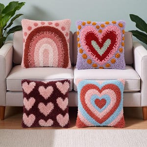 Puede incluir: Cuatro cojines decorativos con diseños texturizados y tupidos. Uno presenta un arcoíris, otro un corazón y otros dos tienen patrones de corazón. Los cojines son en tonos de rosa, rojo, morado y azul, dispuestos sobre un sofá claro.