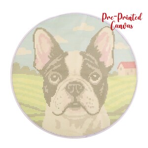Op de afbeelding: Ronde, voorgedrukte canvas met een Franse Bulldog. De hond heeft een zwart-witte vacht met roze oren, tegen een achtergrond van een groen veld, blauwe lucht en een klein huis met een rood dak. De tekst "Pre-Printed Canvas" is rood.