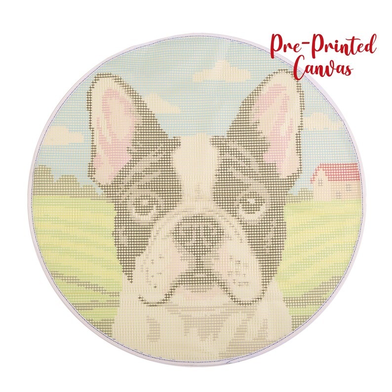 Op de afbeelding: Ronde, voorgedrukte canvas met een Franse Bulldog. De hond heeft een zwart-witte vacht met roze oren, tegen een achtergrond van een groen veld, blauwe lucht en een klein huis met een rood dak. De tekst "Pre-Printed Canvas" is rood.