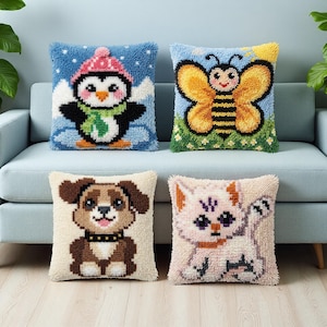 May include: Four square throw pillows with embroidered animal designs. The pillows feature a penguin in a pink hat, a bee, a dog with a black collar, and a pink cat. The pillows are on a light blue sofa.