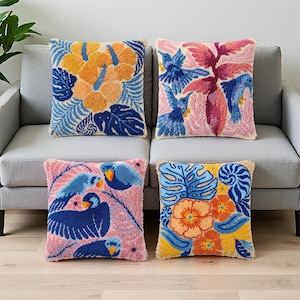 Puede incluir: Cuatro cojines cuadrados con coloridos diseños florales y de pájaros. Los cojines presentan un aspecto texturizado y afelpado con un fondo crema. Los diseños incluyen flores naranjas y amarillas, hojas azules y pájaros rosas.