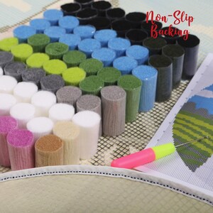 Op de afbeelding: Een kleurrijke tapijthaakset met een verscheidenheid aan garenkleuren, waaronder roze, wit, grijs, groen, blauw en zwart. De set bevat een antislip achterkant, een haak en een patroon. De tekst "Non-Slip Backing" is zichtbaar.