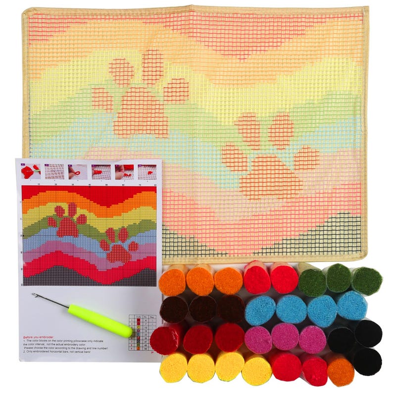 May include: A colorful rainbow-themed needlepoint kit with a design of two paw prints. The kit includes a canvas, yarn, a needle, and instructions. "Before you embroider:" 1. The color boxes on the spot printing showcase only the color number. 2. Please choose the color according to the drawing and the number on the color box. 3. Only embroidered horizontal lines, not vertical ones.