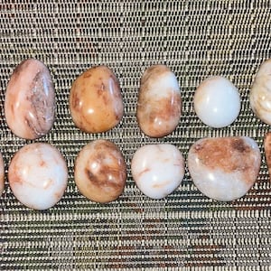 May include: Twelve smooth, polished stones with a mix of white and brown colors. The stones are arranged in two rows of six.