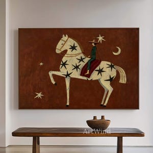 May include: A framed artwork shows a white horse with black star patterns, ridden by a figure in green and red clothing. The background is a dark brown with stars and a crescent moon. The artwork hangs above a wooden bench.