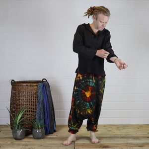 May include: A person wearing a black long-sleeved shirt with a tie-dye pattern on the sleeves and a pair of colorful tie-dye pants. The pants have a large circular pattern in shades of red, orange, yellow, blue, and green.