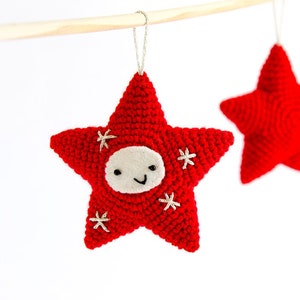 Pode incluir: Enfeite de estrela vermelha de croch&ecirc; com um rosto sorridente e detalhes bordados. A estrela tem um rosto de feltro branco e pequenos detalhes de estrelas brancas. Uma corda prateada &eacute; presa para pendurar. Uma segunda estrela vermelha &eacute; vis&iacute;vel.