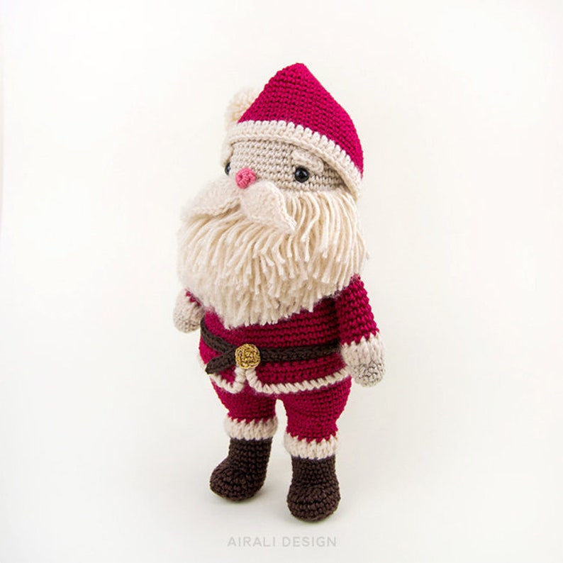 May include: A crocheted Santa Claus doll with a red hat, white beard, and red and white suit. The doll is standing on a white background.