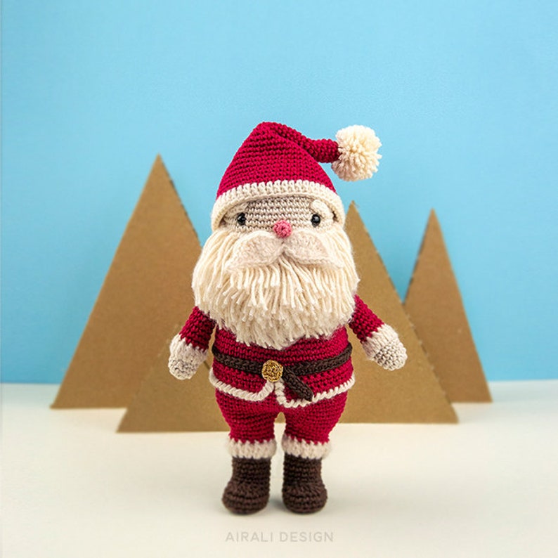May include: A crocheted Santa Claus doll with a red hat, white beard, and red and white suit. The doll is standing in front of a blue background.