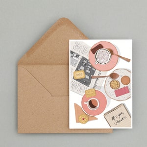 May include: A pink and white card with a handwritten message that says "Miss you, sweetie". The card features an illustration of a cup of coffee, biscuits, and a newspaper with the words "New York Times" printed on it.