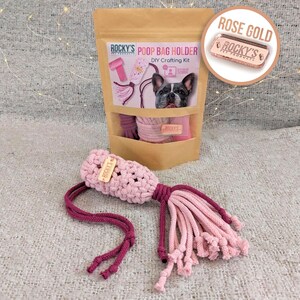 May include: A pink and burgundy crocheted poop bag holder with a "ROCKY'S PET PRODUCTS" tag. The holder is packaged in a brown paper bag with a picture of a French Bulldog and the text "POOP BAG HOLDER DIY Crafting Kit".
