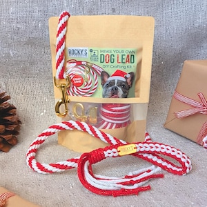 Puede incluir: Un kit de manualidades para correa de perro con cuerda roja y blanca y herrajes dorados. El kit incluye una bolsa con la imagen de un perro con un gorro de Papá Noel y el texto "Make Your Own Dog Lead".