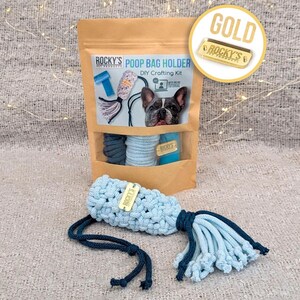 May include: A DIY poop bag holder crafting kit with a blue and gray rope, a blue tag that says "ROCKY'S PET PRODUCTS", and a small tag that says "WITH MY OWN TWO PAWS". The kit is packaged in a brown paper bag with the words "POOP BAG HOLDER" and "DIY Crafting Kit" printed on it. The bag also features a picture of a French Bulldog.