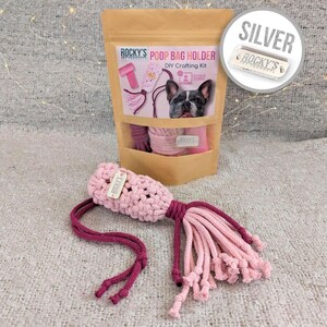 May include: A pink and burgundy crocheted poop bag holder with a silver "ROCKY'S PET PRODUCTS" tag. The holder is a DIY crafting kit and comes with instructions. The image also shows a bag of the kit with a picture of a French Bulldog on the front.