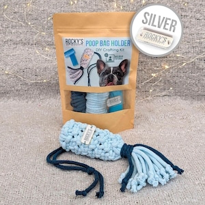 May include: A DIY poop bag holder crafting kit with a blue and gray rope, a silver tag that says "ROCKY'S PET PRODUCTS", and a blue tag that says "ROCKY'S". The kit is packaged in a brown paper bag with a picture of a French Bulldog on the front. The bag also includes instructions for making the poop bag holder.