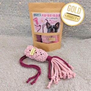 May include: A pink and burgundy crocheted poop bag holder with a gold tag that says "ROCKY'S PET PRODUCTS". The holder is packaged in a brown paper bag with the text "ROCKY'S PET PRODUCTS POOP BAG HOLDER DIY Crafting Kit".
