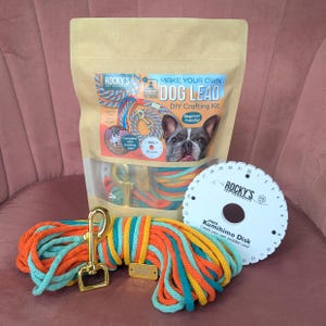 May include: A dog lead DIY crafting kit featuring orange, teal, and yellow rope, a gold-coloured clasp, and a mini Kumihimo disk. The kit includes a bag with the text "MAKE YOUR OWN DOG LEAD" and a dog image.