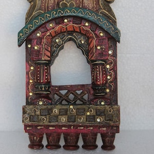 May include: A hand-painted wooden wall decor with intricate details. The piece features a carved archway with a checkered pattern and a red, green, and gold color scheme.