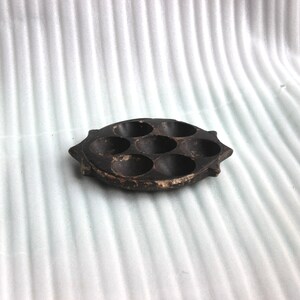 Op de afbeelding: Een zwarte, ronde, stenen of metalen dienblad met zes ronde inkepingen. Het dienblad heeft een licht verhoogde rand en een getextureerd oppervlak.