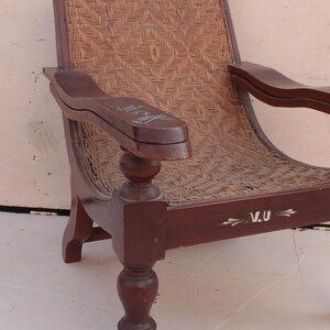 Op de afbeelding: Een donkerbruine houten fauteuil met een gevlochten rieten zitting en rugleuning. De stoel heeft gedraaide poten en een gesneden armleuning. De zitting is gemarkeerd met de initialen "V.U."