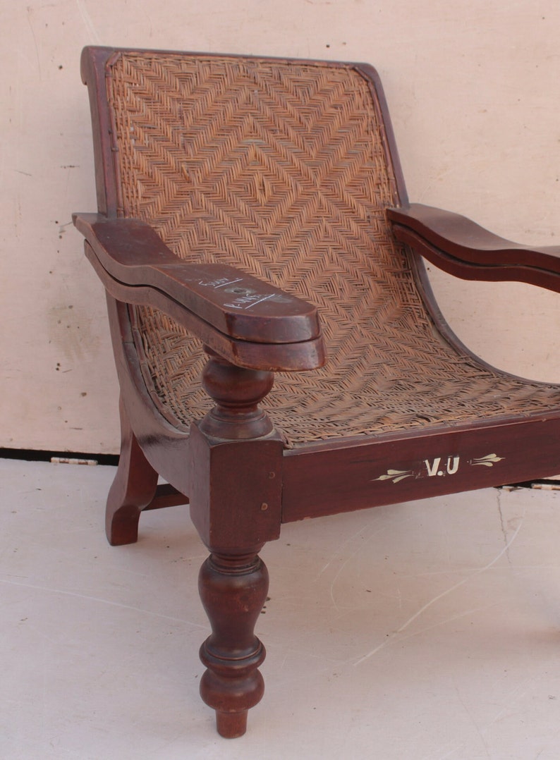 Op de afbeelding: Een donkerbruine houten fauteuil met een gevlochten rieten zitting en rugleuning. De stoel heeft gedraaide poten en een gesneden armleuning. De zitting is gemarkeerd met de initialen "V.U."