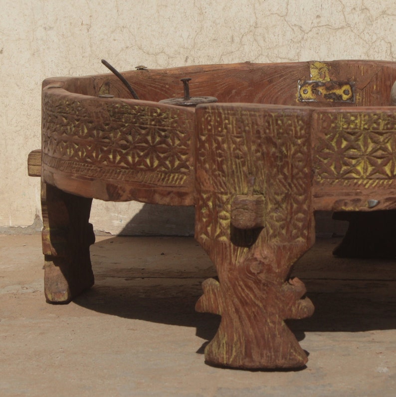 Pu&ograve; includere: Un tavolo rotondo in legno con intagli intricati e una finitura dipinta di giallo. Il tavolo ha quattro gambe intagliate in uno stile decorativo. Il tavolo &egrave; in legno scuro e ha un aspetto rustico.