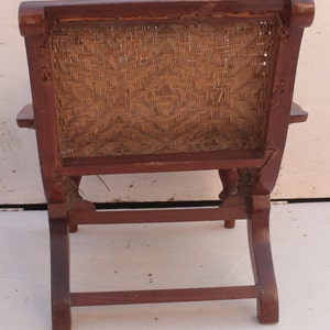 Op de afbeelding: Een houten stoel met een gevlochten rieten zitting en rugleuning. De stoel heeft een eenvoudig ontwerp met een gebogen rugleuning en vier poten.