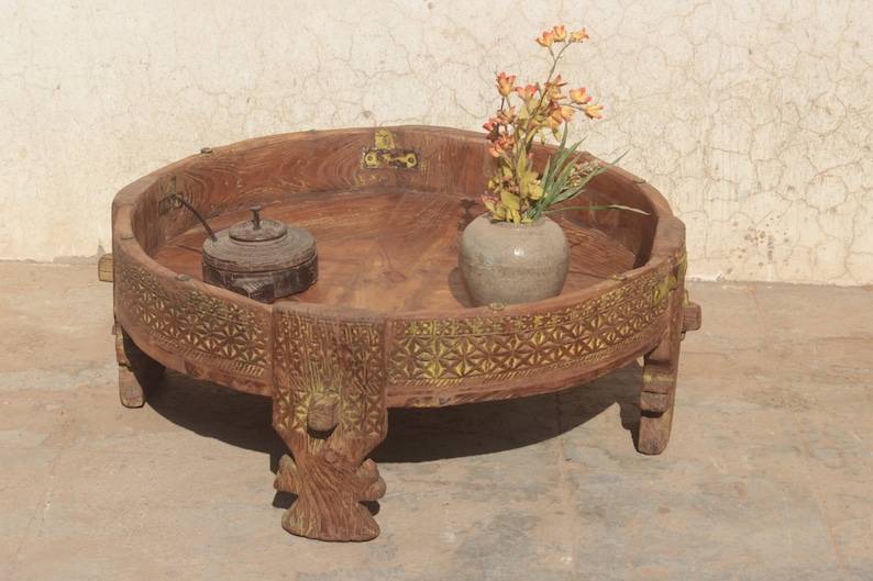 Pu&ograve; includere: Un tavolo rotondo in legno con intagli intricati e un bordo dipinto di giallo. Il tavolo ha quattro gambe ed &egrave; decorato con un piccolo vaso di fiori e un piccolo contenitore di legno.