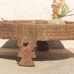 Pu&ograve; includere: Un tavolo rotondo in legno con intagli intricati e una finitura di vernice gialla. Il tavolo ha quattro gambe ed &egrave; decorato con un arrangiamento floreale in un vaso di ceramica.