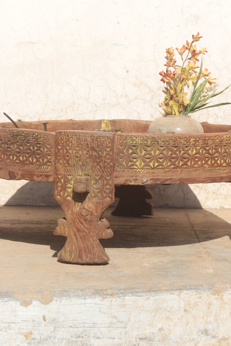 Pu&ograve; includere: Un tavolo rotondo in legno con intagli intricati e una finitura di vernice gialla. Il tavolo ha quattro gambe ed &egrave; decorato con un arrangiamento floreale in un vaso di ceramica.
