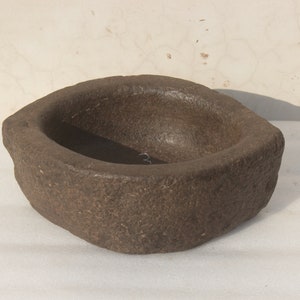 May include: A dark brown, oval-shaped stone mortar with a rough, textured surface. The mortar is designed for grinding and crushing ingredients.