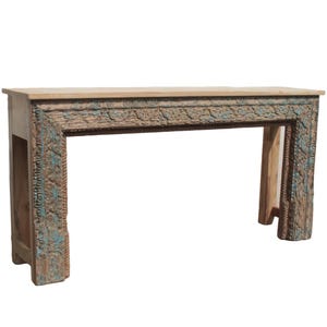 May include: A wooden console table with intricate carvings and a light brown top. The frame features detailed floral and geometric patterns with hints of blue and brown paint, adding a rustic charm. The table is a long, rectangular shape.