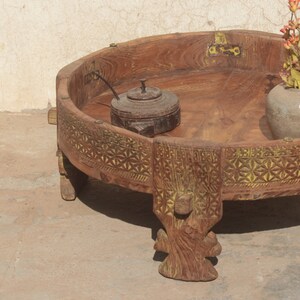 Pu&ograve; includere: Un tavolo rotondo in legno con intricate sculture attorno al bordo. Il tavolo ha quattro gambe che sono anche scolpite e dipinte di giallo. Il tavolo &egrave; in legno scuro e ha un aspetto rustico.