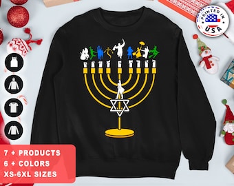 May include: Black sweatshirt featuring a gold menorah and a Star of David. The menorah has seven candles and is surrounded by a group of cartoon figures.