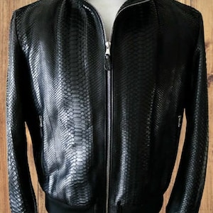 Op de afbeelding: Een zwarte leren bomberjack met een ritssluiting en een slangenhuidpatroon.