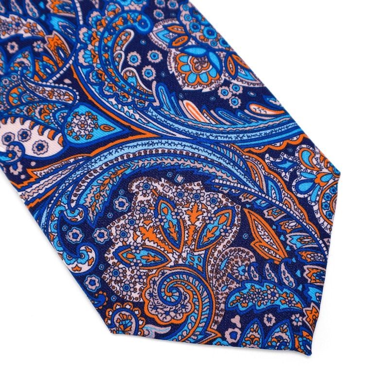 May include: A blue, orange, and white paisley patterned tie. The tie has a pointed end and is made of a silky fabric.