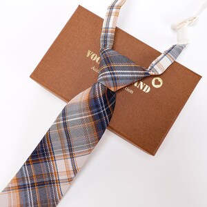 May include: A white, brown, and blue plaid tie with a brown box that says "VOOLAND" and "Acc. Collection".