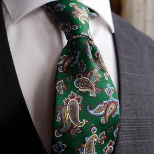 May include: A green paisley tie with a repeating pattern of colorful teardrop-shaped motifs. The tie is knotted and worn with a white collared shirt and a gray suit jacket. The paisley design includes red, blue, and gold accents.