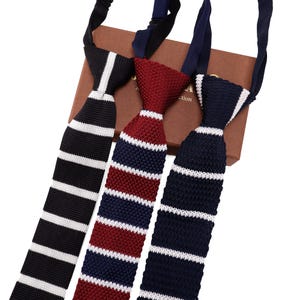 Peut inclure: Trois cravates tricotées noires, bordeaux et bleu marine avec des rayures blanches. Les cravates sont présentées sur une boîte marron. Les cravates ont un aspect texturé et conviennent aux tenues formelles ou professionnelles.