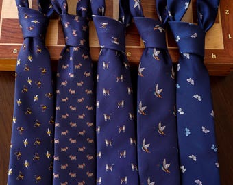 May include: Five navy blue neckties with various patterns, including birds, dogs, and butterflies. The ties are arranged on a wooden surface, showcasing their different designs and colors. Each tie has a unique pattern, offering a variety of styles.