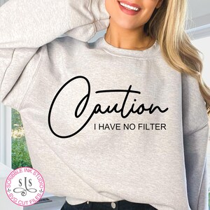 Könnte beinhalten: Ein graues Sweatshirt mit dem Text "Caution I Have No Filter" in schwarzer Kursivschrift.