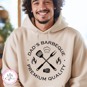 May include: A beige hoodie with a black circle graphic that says "Dad's Barbeque. Premium Quality." The graphic includes a chef's hat, crossed grilling tools, and flames.