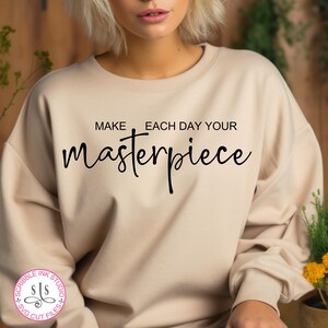 May include: A beige sweatshirt with the text "Make each day your masterpiece" printed in black.
