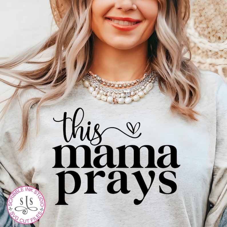 May include: A white t-shirt with the text "this mama prays" in black lettering with a small heart above the word "mama".