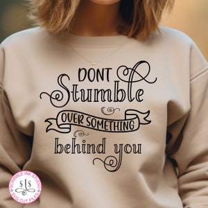 Pode incluir: Uma camisa de moletom bege com texto preto que diz "Não tropece em algo que está atrás de você".