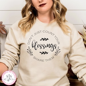 May include: A beige sweatshirt with a black circle graphic that says "Don't just count your blessings, share them".